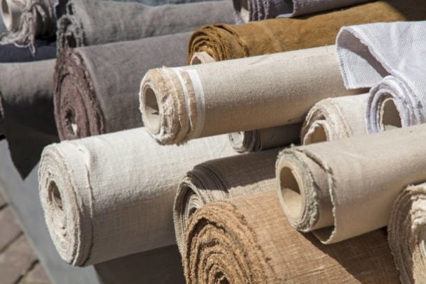 Close up assorted rolls of white, beige and brown flax linen fabric and canvas textile on retail market stall, high angle view